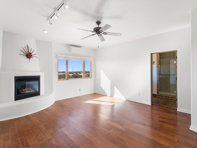 unfurnished living room with a glass covered fireplace, a wall unit AC, wood finished floors, and baseboards