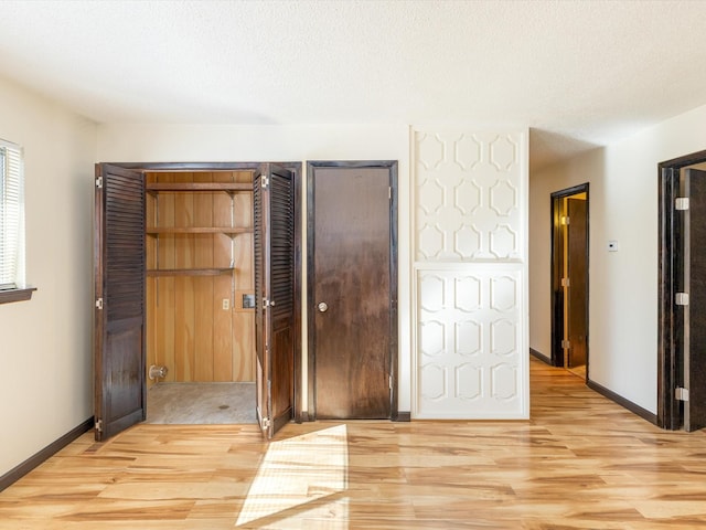 unfurnished bedroom featuring light wood-style floors, baseboards, and a textured ceiling