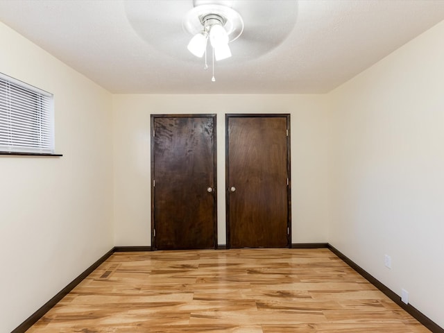 unfurnished bedroom featuring a ceiling fan, baseboards, light wood finished floors, and two closets