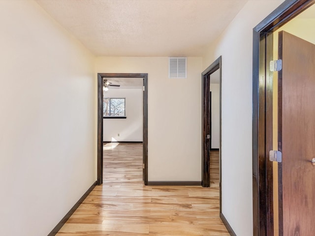 corridor featuring light wood-style floors, baseboards, visible vents, and a textured ceiling