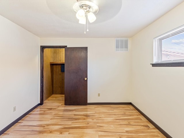 spare room with light wood-type flooring, visible vents, ceiling fan, and baseboards