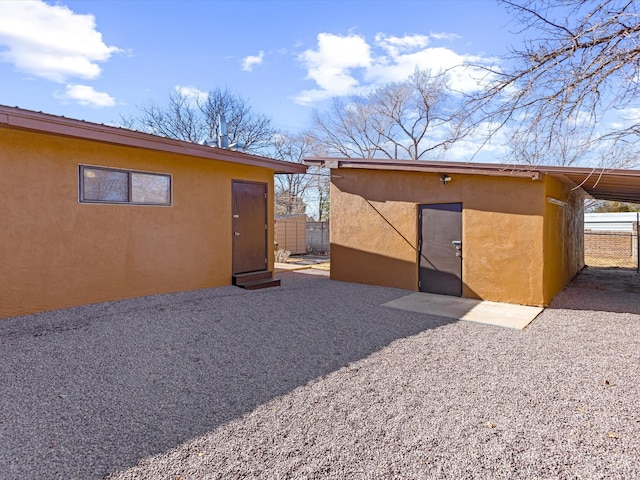 rear view of house featuring fence, an outdoor structure, and stucco siding