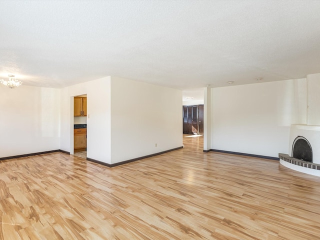 unfurnished living room with a textured ceiling, a fireplace, baseboards, light wood finished floors, and an inviting chandelier