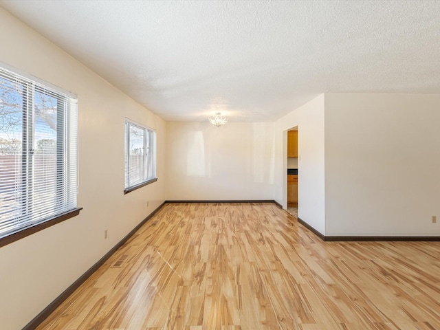 empty room with light wood-style flooring, baseboards, a chandelier, and a textured ceiling