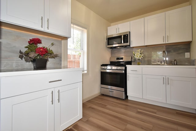 kitchen with sink, light hardwood / wood-style flooring, white cabinetry, stainless steel appliances, and tasteful backsplash