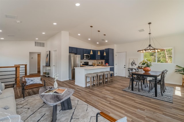 living room with vaulted ceiling, sink, an inviting chandelier, and light hardwood / wood-style floors