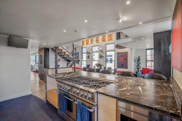 kitchen with light brown cabinetry, stainless steel appliances, and dark stone countertops