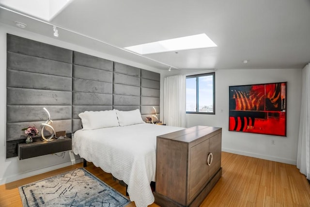 bedroom with light hardwood / wood-style flooring, track lighting, and a skylight