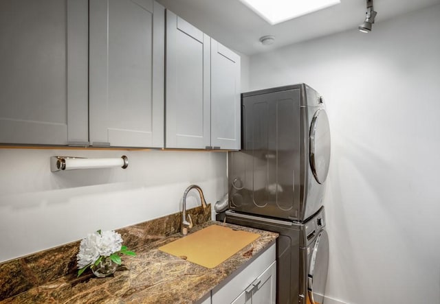 laundry room with cabinets, stacked washing maching and dryer, sink, and rail lighting