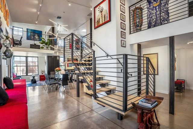 stairway with a towering ceiling, concrete flooring, and rail lighting