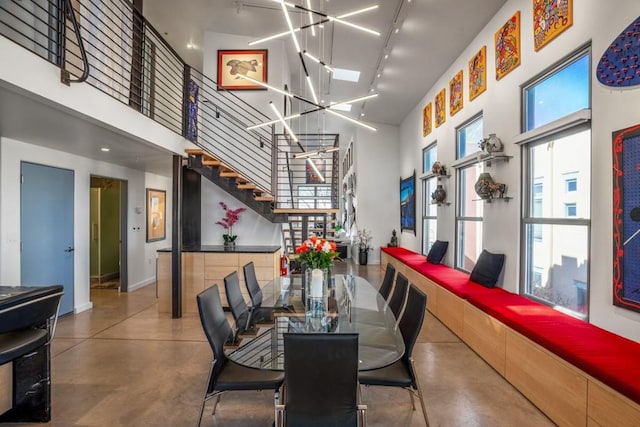 dining space with an inviting chandelier, a towering ceiling, track lighting, and concrete floors