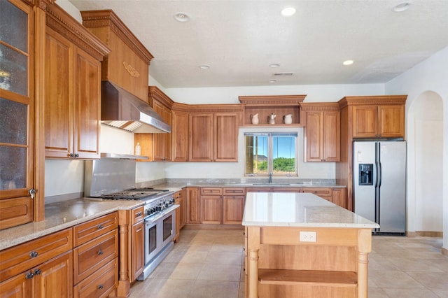 kitchen with wall chimney exhaust hood, sink, a center island, light tile patterned floors, and stainless steel appliances