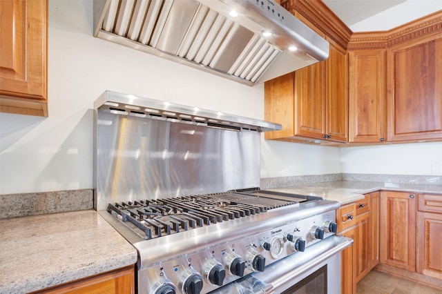 kitchen featuring light stone counters, light tile patterned flooring, stainless steel stove, and exhaust hood