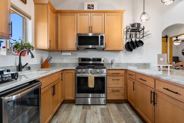 kitchen featuring sink, stainless steel appliances, decorative light fixtures, beverage cooler, and light wood-type flooring