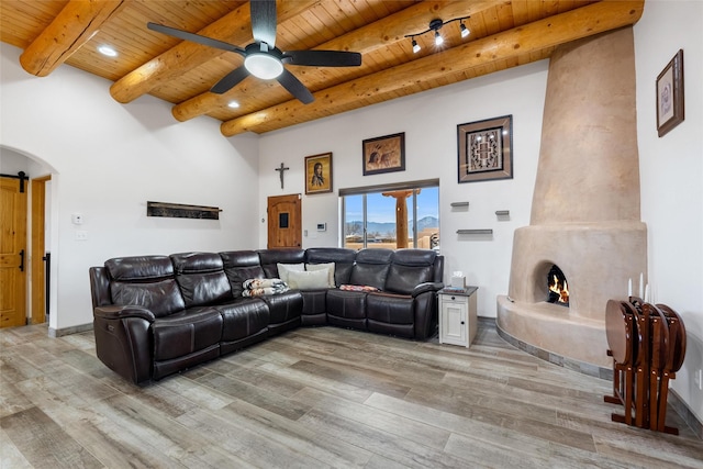 living room with a fireplace, ceiling fan, wooden ceiling, beam ceiling, and light hardwood / wood-style flooring