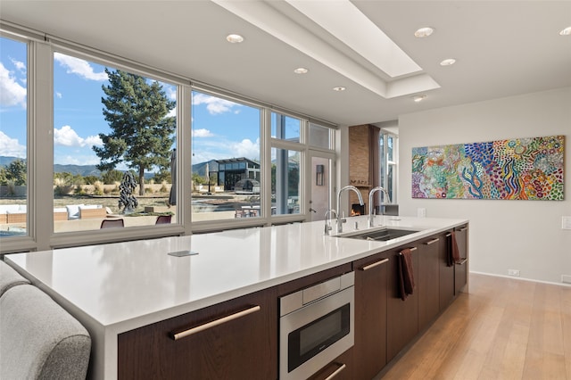 kitchen featuring sink, light hardwood / wood-style flooring, a kitchen island with sink, dark brown cabinets, and stainless steel microwave