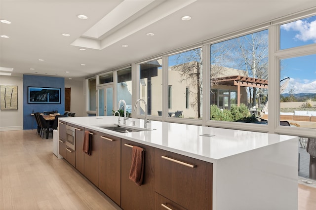 kitchen featuring stainless steel microwave, a skylight, sink, a center island with sink, and light wood-type flooring