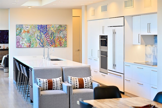 kitchen with a breakfast bar, sink, white cabinetry, tasteful backsplash, and a center island with sink