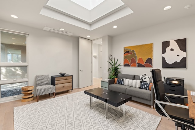 living room with light hardwood / wood-style flooring, a tray ceiling, and a skylight