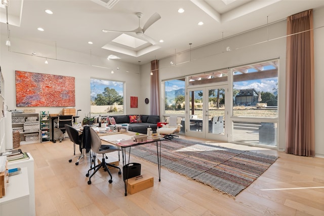 home office with a skylight, a high ceiling, ceiling fan, light wood-type flooring, and french doors