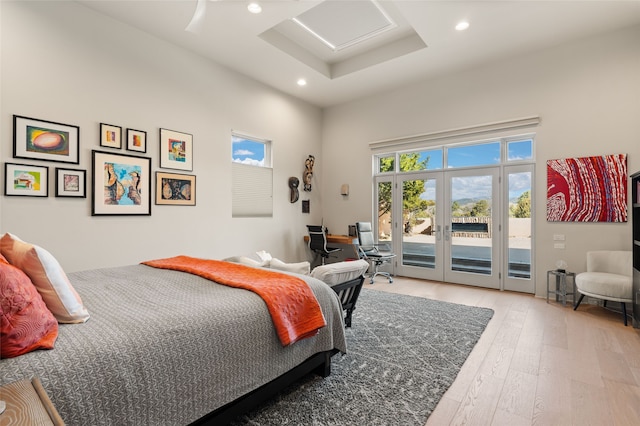 bedroom with french doors, light hardwood / wood-style flooring, access to outside, a raised ceiling, and a towering ceiling