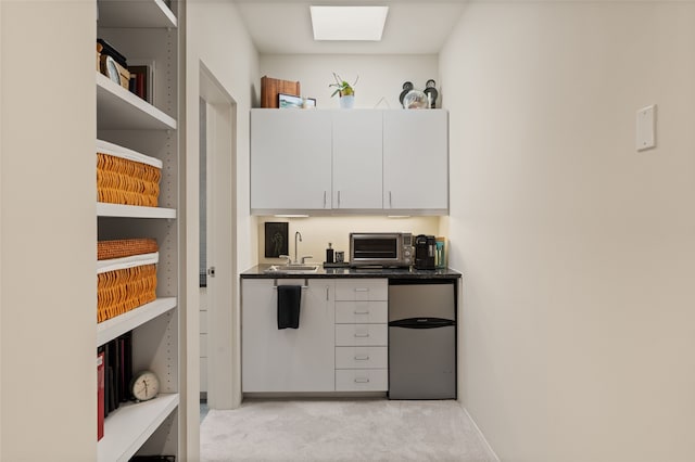 kitchen featuring sink, stainless steel refrigerator, a skylight, white cabinets, and light colored carpet