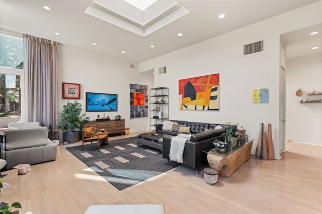 living room featuring a towering ceiling, a skylight, and light hardwood / wood-style flooring