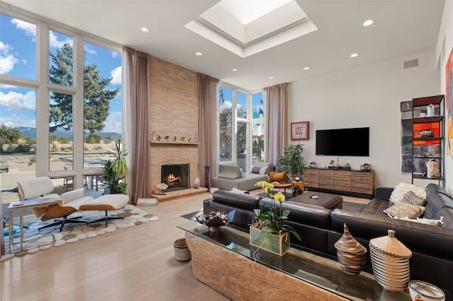 living room with expansive windows, light wood-type flooring, a fireplace, and a skylight