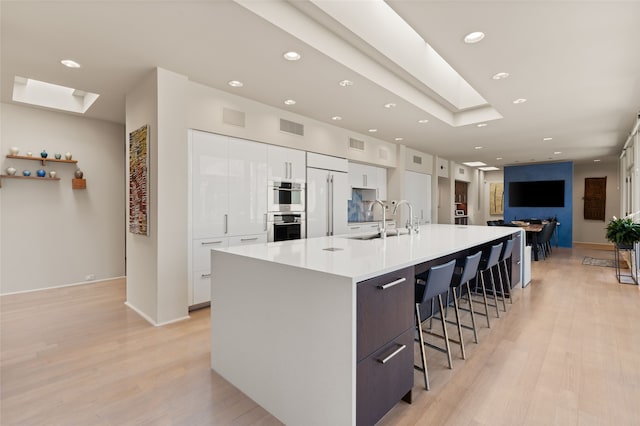 kitchen featuring white cabinetry, sink, a skylight, and a spacious island