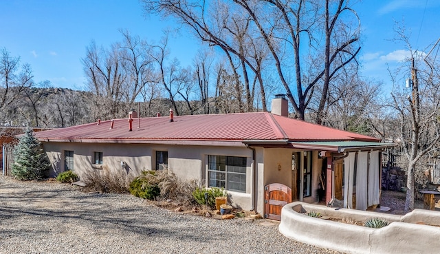 view of front facade with metal roof, a chimney, and stucco siding