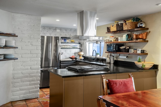 kitchen featuring island exhaust hood, open shelves, dark countertops, freestanding refrigerator, and a sink