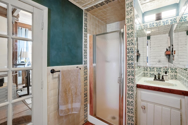 full bath with a stall shower, vanity, and tile walls