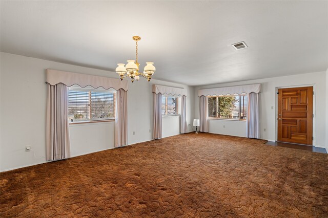 carpeted empty room featuring an inviting chandelier