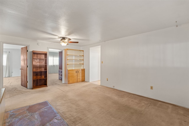 unfurnished living room with ceiling fan, light colored carpet, and a textured ceiling