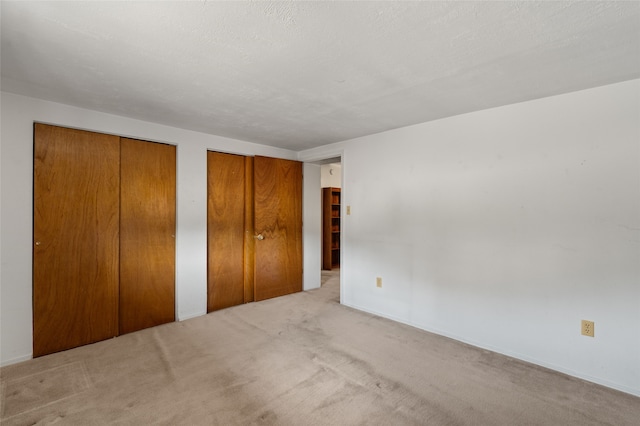 unfurnished bedroom with two closets, light colored carpet, and a textured ceiling