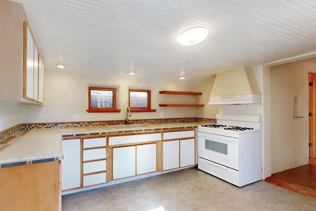 kitchen featuring sink, custom exhaust hood, gas range gas stove, tile counters, and white cabinets