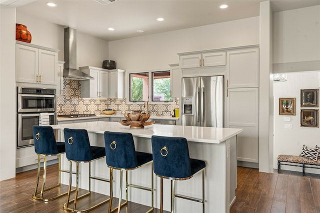 kitchen with tasteful backsplash, a center island, appliances with stainless steel finishes, a kitchen breakfast bar, and wall chimney range hood