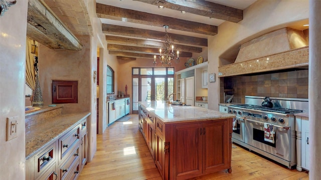 kitchen with pendant lighting, a kitchen island with sink, tasteful backsplash, custom exhaust hood, and range with two ovens