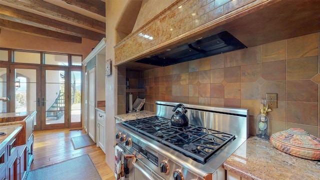 kitchen with stainless steel stove, backsplash, light hardwood / wood-style floors, light stone countertops, and french doors