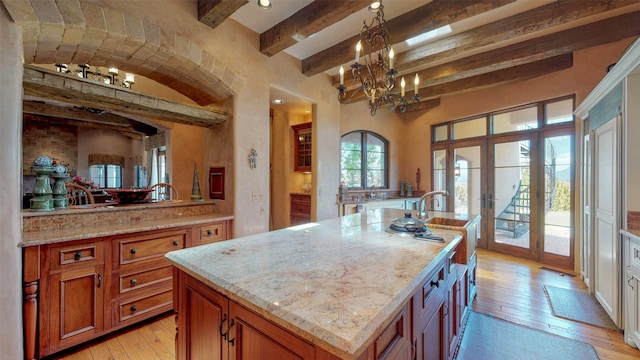 kitchen with pendant lighting, a kitchen island with sink, light hardwood / wood-style floors, beam ceiling, and french doors