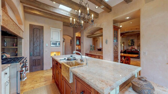 kitchen with sink, appliances with stainless steel finishes, a kitchen island with sink, beam ceiling, and light wood-type flooring