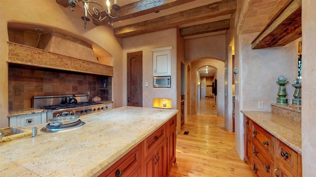 kitchen with beam ceiling, stainless steel appliances, tasteful backsplash, light stone counters, and light hardwood / wood-style floors