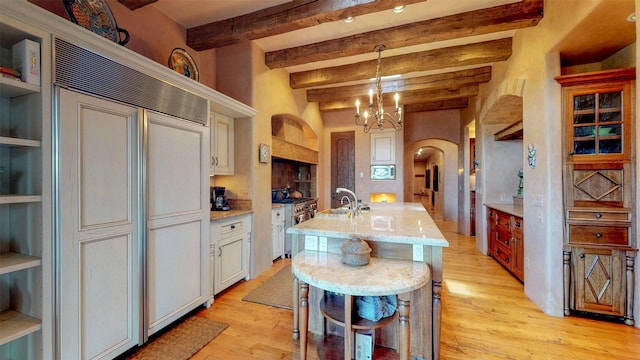 kitchen featuring a breakfast bar, a kitchen island with sink, hanging light fixtures, a notable chandelier, and light wood-type flooring