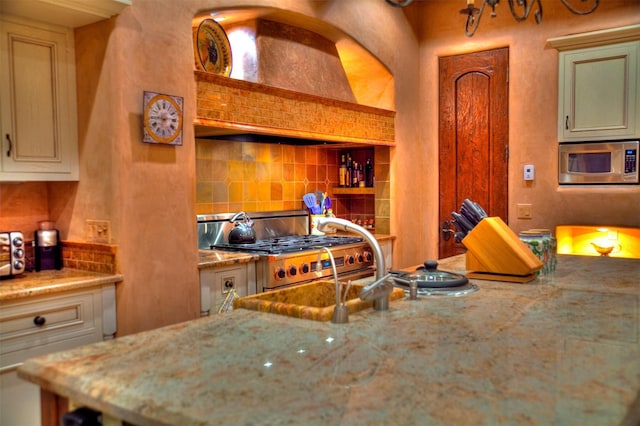 kitchen with stainless steel appliances, custom exhaust hood, light stone countertops, and decorative backsplash