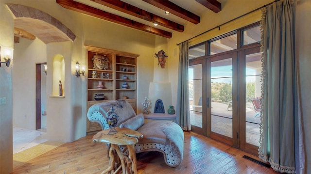 living area with beam ceiling, light hardwood / wood-style flooring, and french doors