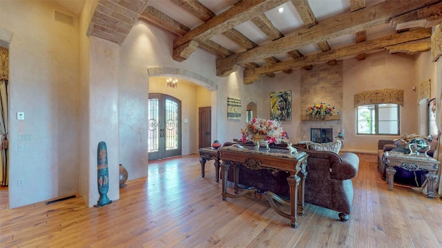 interior space featuring a fireplace, beamed ceiling, a high ceiling, light hardwood / wood-style floors, and french doors