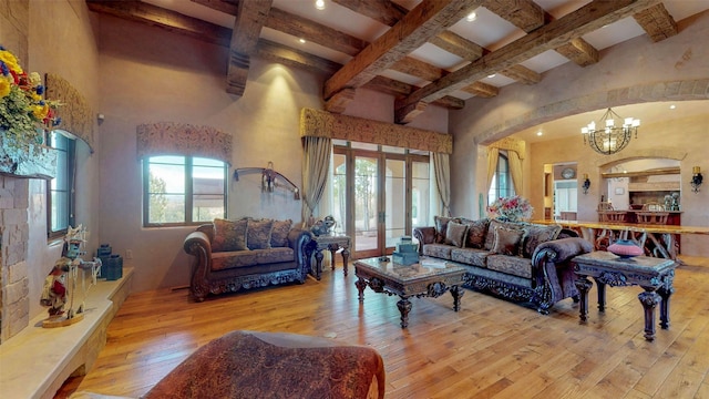 living room featuring a notable chandelier, beam ceiling, a towering ceiling, and light wood-type flooring