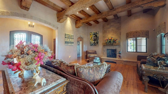 living room featuring a high ceiling, a fireplace, light hardwood / wood-style floors, and beamed ceiling