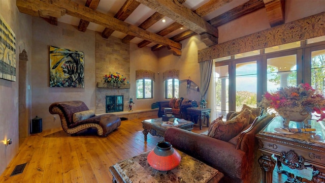 living room featuring beamed ceiling, a fireplace, a high ceiling, and light wood-type flooring