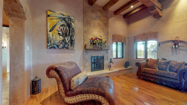 living room with beamed ceiling, a stone fireplace, light hardwood / wood-style floors, and a high ceiling